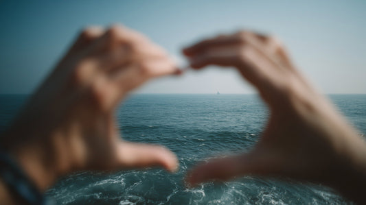 A first-person view of hands framing the blue ocean and a tiny sailboat on the horizon.